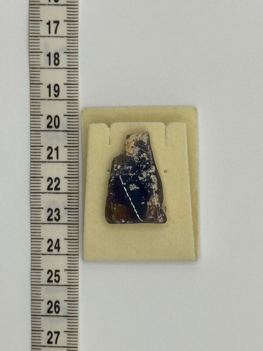 Natural Australian opal embedded in host rock, small specimen displayed next to ruler for size reference.
